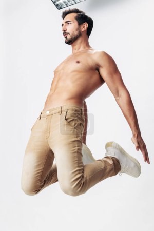 Foto de Modelo de moda masculina con un torso desnudo y abdominales paquetes saltando sobre un fondo blanco aislado, estilo de ropa de moda, espacio de copia, espacio para el texto. Foto de alta calidad - Imagen libre de derechos