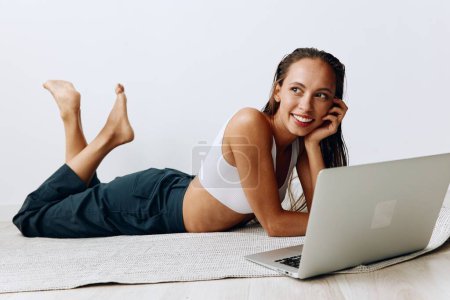 Foto de Una mujer se acuesta en el suelo en casa y sonríe con los dientes mientras mira una computadora portátil mientras charla en línea y ve programas de televisión en su día libre. Foto de alta calidad - Imagen libre de derechos