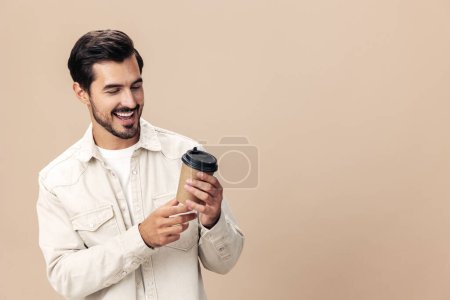 Foto de Retrato de un hombre con estilo con un vaso de café consigo mismo maqueta sobre un fondo beige en una camiseta blanca, estilo de ropa de moda, espacio. Foto de alta calidad - Imagen libre de derechos