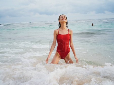 Téléchargez les photos : Modèle féminin sexy en maillot de bain rouge avec corps athlétique se tient dans l'eau dans l'océan et pose, l'entretien du corps en vacances. Photo de haute qualité - en image libre de droit