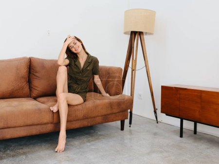 Foto de Mujer joven modelo sentado en el sofá en casa sonriente y relajante, estilo de vida interior moderno, espacio de copia. Foto de alta calidad - Imagen libre de derechos
