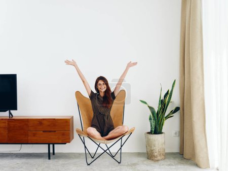 Photo for Woman sitting in a leather armchair near the window hands up smile , modern stylish interior Scandinavian lifestyle, copy space. High quality photo - Royalty Free Image