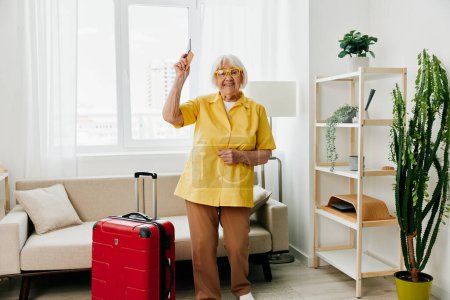 Foto de Mujer mayor feliz con pasaporte y billete de viaje hizo una maleta roja, vacaciones y atención médica. Foto de alta calidad - Imagen libre de derechos
