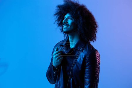 Photo for Portrait of fashion man with curly hair on blue background multinational, colored light, black leather jacket trend, modern concept. High quality photo - Royalty Free Image
