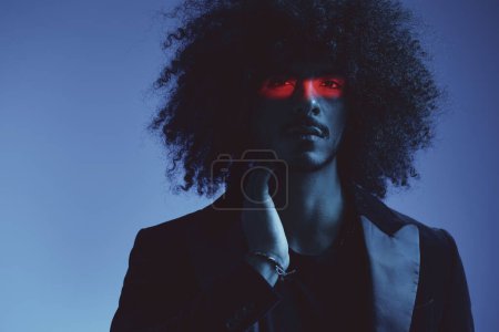 Foto de Retrato de moda de un hombre con el pelo rizado sobre un fondo azul con una franja roja de luz, luz multicolor, moderno concepto de moda. Foto de alta calidad - Imagen libre de derechos