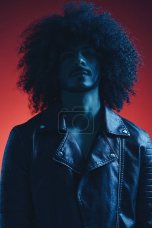 Photo for Portrait of fashion man with curly hair on red background multinational, colored light, black leather jacket trend, modern concept. High quality photo - Royalty Free Image
