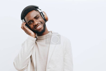 Téléchargez les photos : Homme coloré beige écouteurs attrayant noir afro guy confiant studio beau joie portrait américain dj visage style mode musique posant fond africain - en image libre de droit
