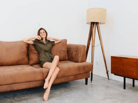 Photo for Young woman model sitting on the couch at home smiling and relaxing, modern interior lifestyle. High quality photo - Royalty Free Image