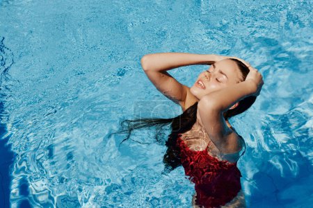 Téléchargez les photos : Femme heureuse nageant dans la piscine en maillot de bain rouge avec les cheveux longs lâches, protection de la peau avec écran solaire, concept de détente en vacances. Photo de haute qualité - en image libre de droit