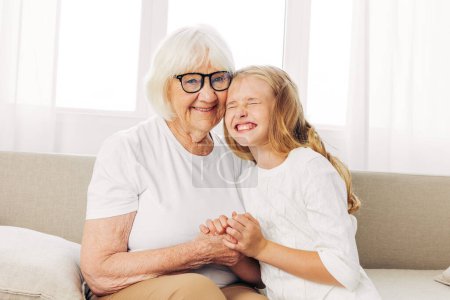 Photo for Woman sofa granddaughter girl mother couch generation love old sitting happy senior child grandmother home elderly hug lifestyle daughter family - Royalty Free Image