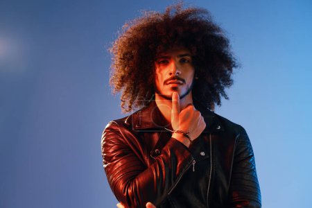 Photo for Portrait of a stylish man with curly hair on a blue background multinational, colored light, black leather jacket trend, modern concept. High quality photo - Royalty Free Image