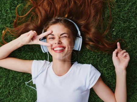 Foto de Feliz adolescente escuchando música con auriculares tumbados en el césped verde en el parque, vacaciones de verano. Foto de alta calidad - Imagen libre de derechos