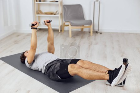 Foto de Hobby hombre gris activo deporte estera ejercicio yoga casa mancuernas ajuste habitación tutorial estilo de vida cuerpo actividad física atleta indoor fitness entrenamiento salud - Imagen libre de derechos