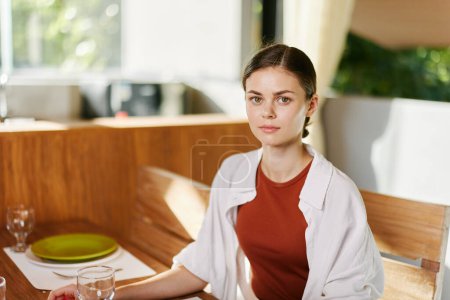 Foto de Mujer elegante sentada en la mesa de comedor bebiendo agua de un vaso, el interior moderno del hogar, la luz del atardecer, el estilo de vida con comodidad. Foto de alta calidad - Imagen libre de derechos