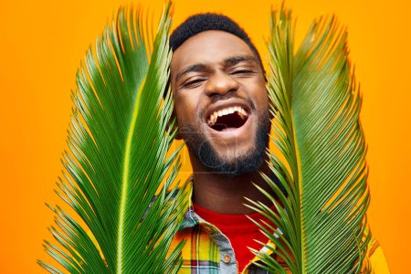 Foto de Hombre sonriente moda africano guapo árbol palma joven amarillo negro elegante etnia feliz tropical colores piel estudio americano masculino divertido expresión camiseta multinacional - Imagen libre de derechos