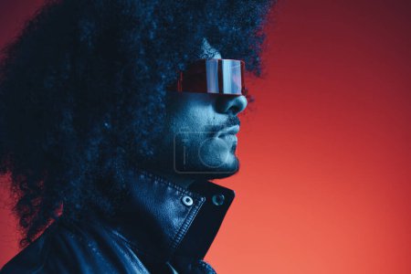 Photo for Portrait of fashion man with curly hair on red background with stylish glasses, multicultural, colored light, black leather jacket trend, modern concept. High quality photo - Royalty Free Image