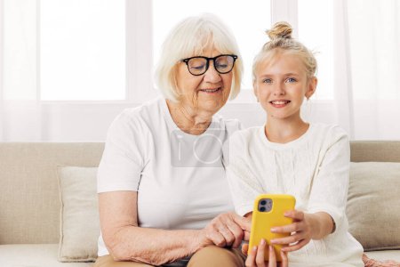 Photo for Two photography education child togetherness selfie granddaughter t-shirt people hugging happiness sofa phone smiling bonding white call copy video indoors grandmother family space - Royalty Free Image