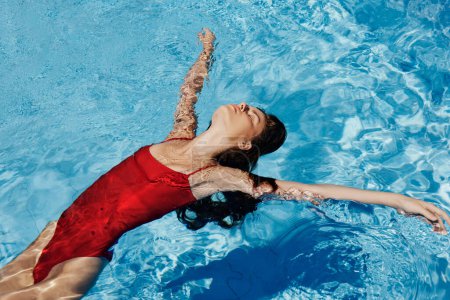 Photo for Happy woman swimming in pool in red swimsuit with loose long hair, skin protection with sunscreen, concept of relaxing on vacation. High quality photo - Royalty Free Image