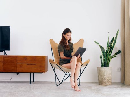 Photo for Female student study sits on a chair with a laptop work at home smile and relax, modern stylish interior Scandinavian lifestyle, copy space. High quality photo - Royalty Free Image