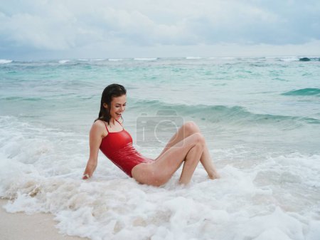Foto de Una mujer en traje de baño rojo se encuentra en la arena junto al océano en las olas en la playa de la isla de Bali. Foto de alta calidad - Imagen libre de derechos