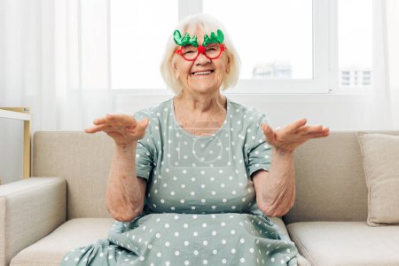 Foto de Mujer sofá gafas maduras feliz sonrisa femenina anciano adulto navidad año retrato caucásico abuela felicidad xmas acogedor pensionista vacaciones casa nuevo - Imagen libre de derechos
