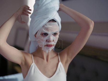 Photo for Young woman lying on bed with moisturizing beauty face mask and white towel on her head after shower, lifestyle home skincare, smile. High quality photo - Royalty Free Image