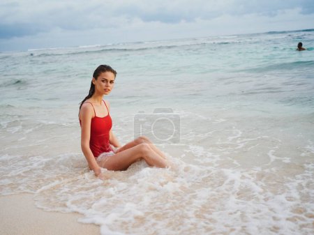 Foto de Una joven con un traje de baño rojo yace en la arena con un hermoso bronceado y mira al océano en los trópicos. Foto de alta calidad - Imagen libre de derechos