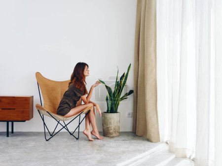Photo for Woman sitting on a chair near the window smiling, modern stylish interior Scandinavian lifestyle, copy space. High quality photo - Royalty Free Image