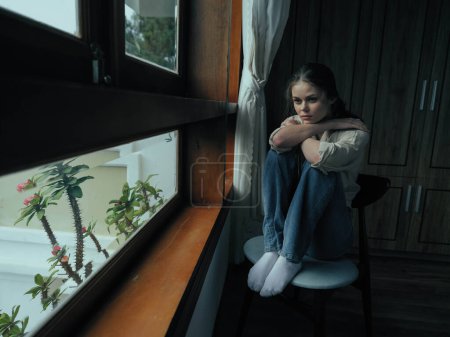 Téléchargez les photos : Femme chute dépression assis par la fenêtre et regardant la nature, temps pluvieux et découragement, style de vie à la maison, solitude. Photo de haute qualité - en image libre de droit