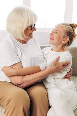 Photo for Woman grandmother senior happy hug sitting sofa bonding girl love elderly granddaughter daughter couch child family lifestyle hugging mother old home - Royalty Free Image