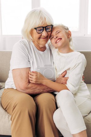 Foto de Abrazando a la mujer nieta niña anciana hija feliz abrazo madre padre niño sofá sofá casa viejo vinculación amor familia estilo de vida abuela - Imagen libre de derechos