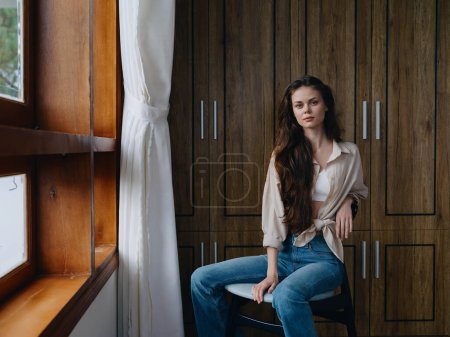 Photo for Woman sitting on a chair in home interior near the window, comfort and coziness, lifestyle relaxation on the weekend, pensive look of a beautiful girl. High quality photo - Royalty Free Image