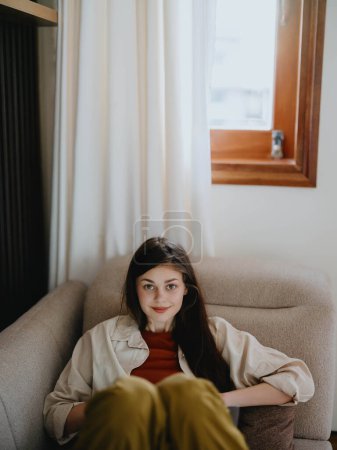 Foto de Una mujer se acuesta en un sofá con un portátil y mira pensativamente a la pantalla entrenando a un freelancer en el trabajo, un estilo de vida real sin retocar. Foto de alta calidad - Imagen libre de derechos