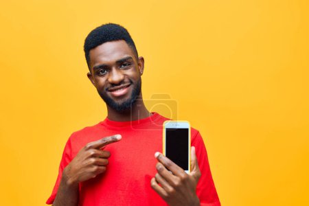 Téléchargez les photos : Homme heureux modèle mobile jaune copie souriant millénaire espace téléphone africain gars mâle branché main maquette noir cellule technologie fond portrait jeune isolé - en image libre de droit