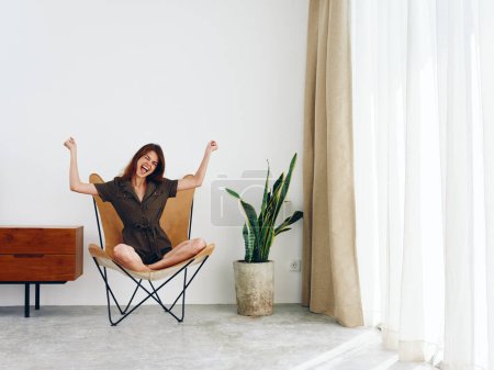 Photo for Woman sitting in a leather armchair near the window smiling , modern stylish interior Scandinavian lifestyle, copy space. High quality photo - Royalty Free Image