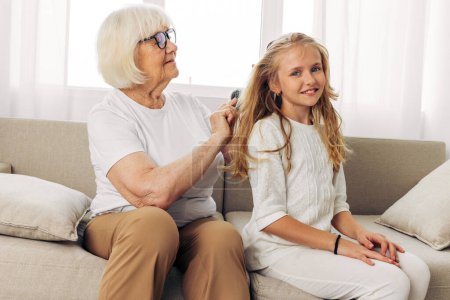 Photo for Happy woman daughter girl grandmother couch combing child elderly home sofa hair senior hug hair love lifestyle mother granddaughter old family comb - Royalty Free Image