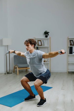 Foto de Hombre entrenamiento yoga pesas ejercicio actividad casa joven atleta interior muscular gimnasio deportivo deporte cuarentena salud estilo de vida bienestar fuerza gris activo - Imagen libre de derechos