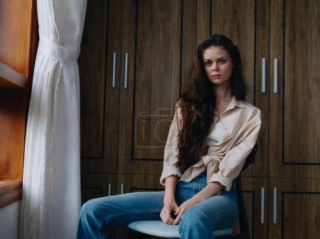 Photo for Woman sitting on a chair in home interior and simple clothes near the window, comfort and coziness, lifestyle relaxation on the weekend, pensive look of a beautiful girl. High quality photo - Royalty Free Image
