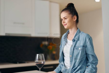 Photo for Solitude and Sorrow: A Depressed Young Woman, Sitting Alone in a Stylish Kitchen, Holding a Glass of Red Wine - Royalty Free Image