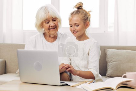 Téléchargez les photos : Bonding grand-mère souriant vidéo ordinateur portable espace éducation petite-fille appeler ensemble à l'intérieur copier enfant blanc photographie canapé selfie famille étreinte t-shirt - en image libre de droit