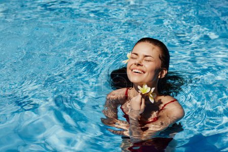 Photo for Young woman in swimming pool in red swimsuit with beautiful smile and Balinese flower in the sun swimming in the pool, concept of relaxation on vacation. High quality photo - Royalty Free Image