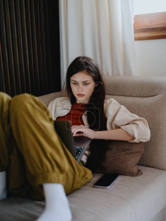 Photo for A woman lies on a couch with a laptop and stares pensively into the screen training a freelancer at work, a real lifestyle without retouching. High quality photo - Royalty Free Image