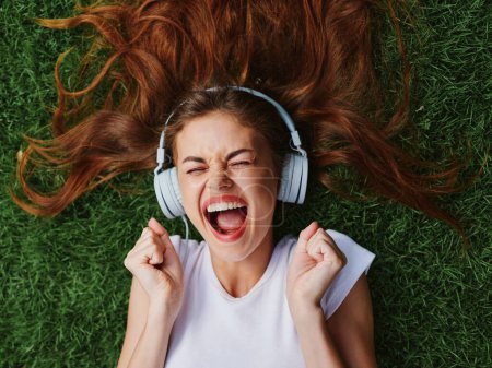 Téléchargez les photos : Bonne adolescente écoutant de la musique avec des écouteurs couchés sur l'herbe verte du parc, vacances d'été. Photo de haute qualité - en image libre de droit