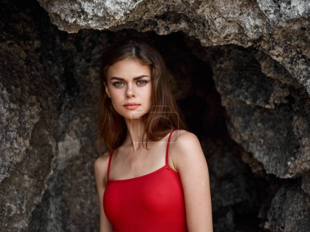 Foto de Retrato de una mujer en traje de baño rojo contra las rocas junto al océano, piel bronceada del sol, el concepto de proteger la piel del sol y la salud corporal. Foto de alta calidad - Imagen libre de derechos