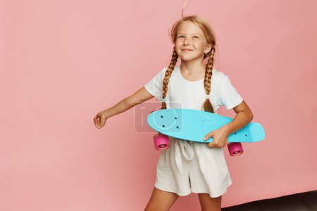 Téléchargez les photos : Mode de vie actif : Adorable petite fille patinant sur un panneau rose vif Penny - en image libre de droit