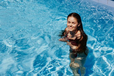 Téléchargez les photos : Femme heureuse nageant dans la piscine en maillot de bain rouge avec les cheveux longs lâches au soleil, protection de la peau avec écran solaire, concept de détente en vacances. Photo de haute qualité - en image libre de droit