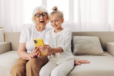Photo for Sofa smiling selfie hugging child phone togetherness granddaughter space grandmother education bonding copy family white call t-shirt photography people two video indoors - Royalty Free Image