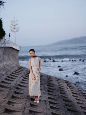 Téléchargez les photos : Seule dans la solitude sereine : Une belle jeune mannequin féminine posant sur un rocher, regardant dans l'océan, profitant d'une soirée d'été relaxante à la plage. - en image libre de droit