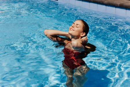 Foto de Mujer feliz nadando en la piscina en traje de baño rojo con pelo largo suelto bajo la luz del sol, protección de la piel con protector solar, concepto de relajarse en vacaciones en clima tropical. Foto de alta calidad - Imagen libre de derechos