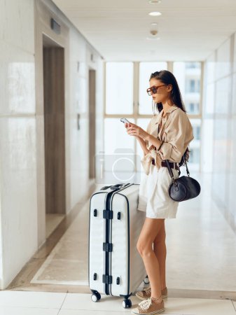 Foto de Viajero alegre: Mujer joven esperando en la terminal del aeropuerto con maleta y bolsa, emocionada por las vacaciones - Imagen libre de derechos